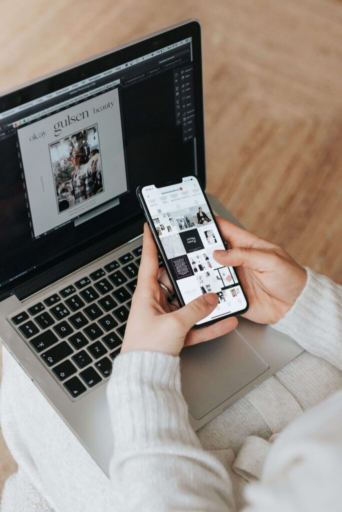 Person using a smartphone and laptop for social media content and digital design work.